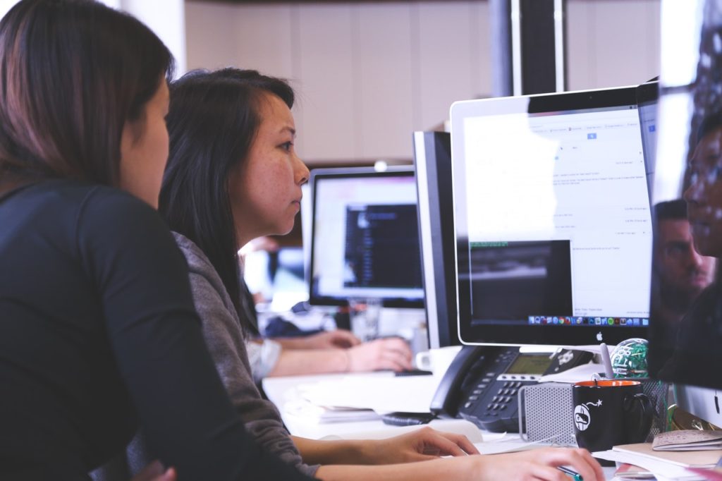 Two women seated at computer workstations in a contemporary office environment, both focused on their screens, representing data analysis and technological coordination related to IoT in smart cities.

Let me know if you want an alternative angle that emphasizes public sector planning or environmental sustainability.