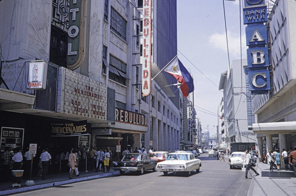 Escolta Street in Manila featuring the Rebullida department store with ornate pre-war architecture beside a vintage movie theater marquee, illustrating historic mixed-use structures that reflect the enduring typology of shophouses in the Philippines.