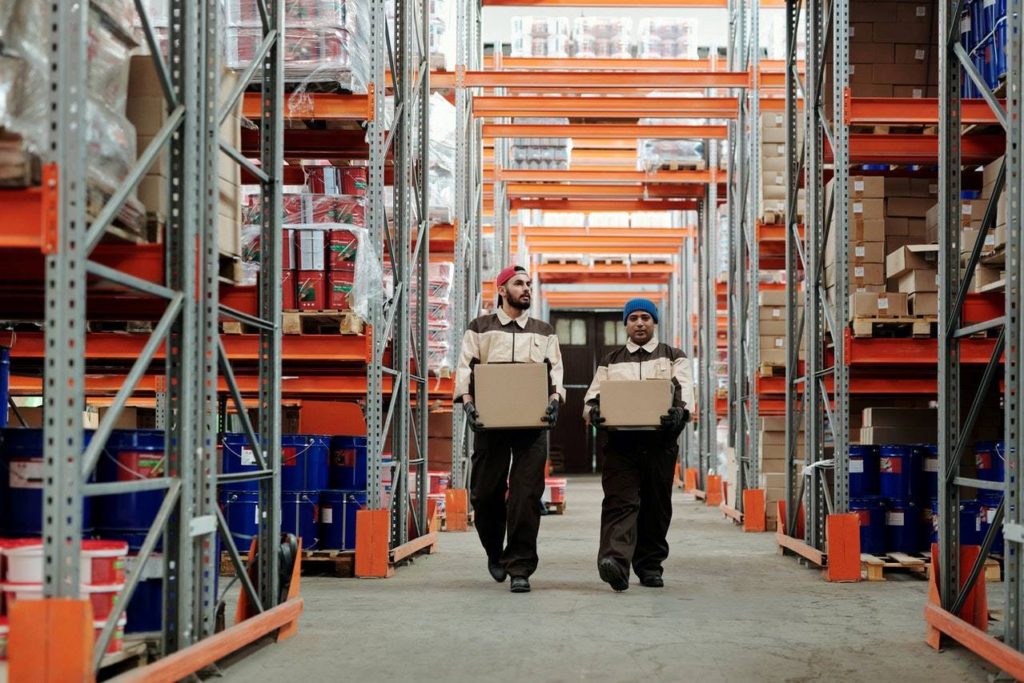 Two workers transporting product inventories in an industrial warehouse.