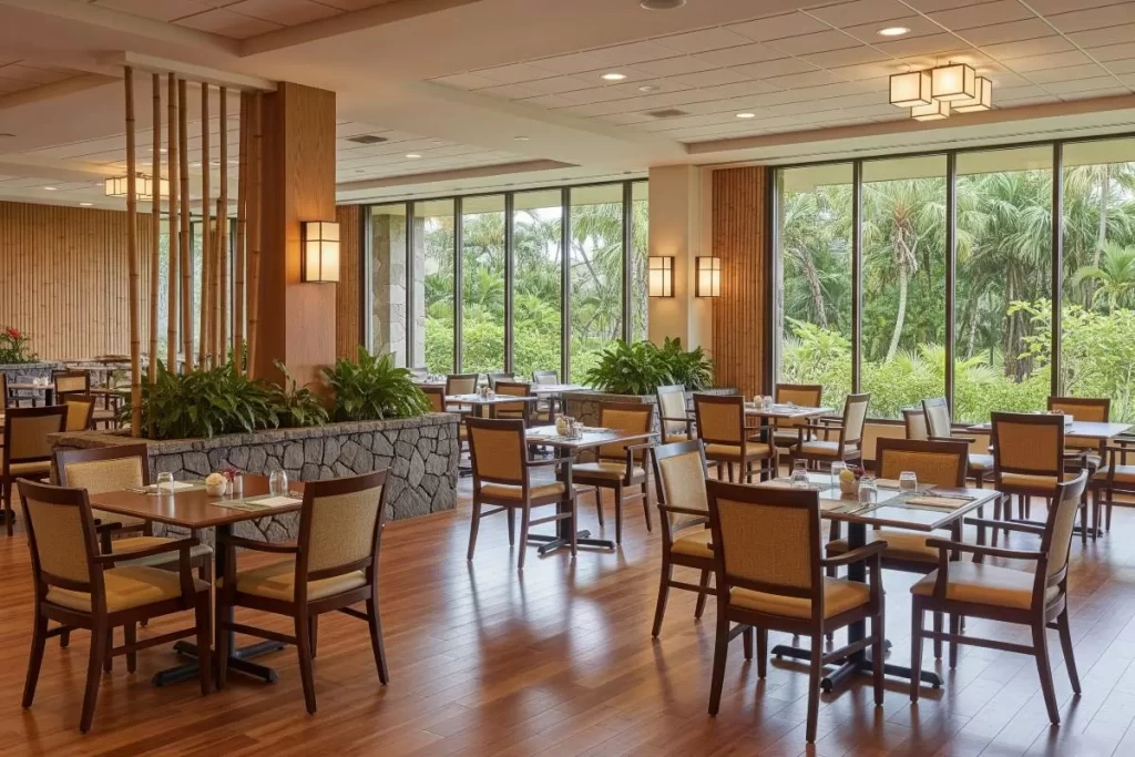 An indoor restaurant with wide circulation spaces, natural light, accessible seating arrangements, and elegant finishes is shown as a communal dining area designed for seniors in a tropical retirement community.