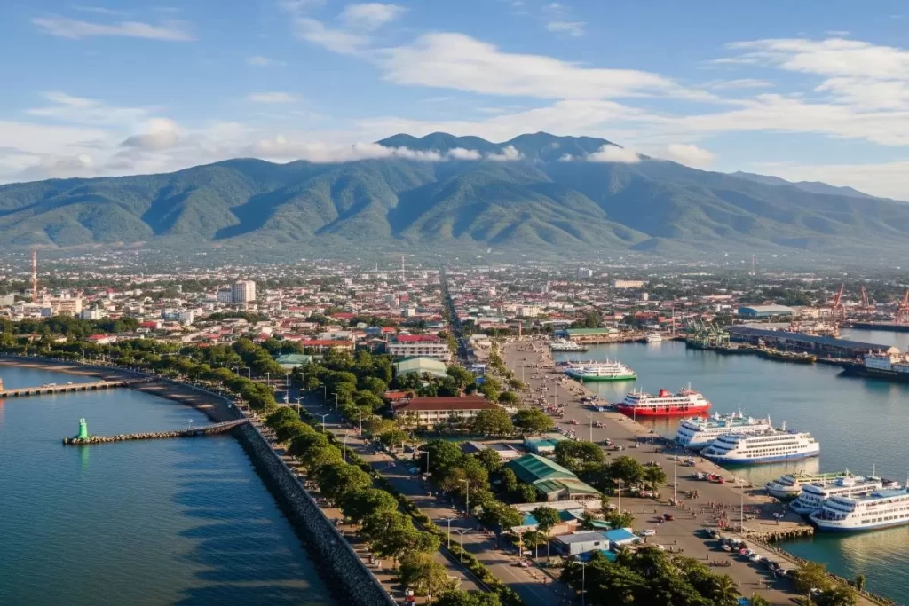 A panoramic view of Dumaguete’s seaside boulevard with stone balustrades, palm-lined walkways, historic colonial buildings, and people strolling along the waterfront under a clear blue sky, showcasing the harmonious blend of coastal scenery and urban architecture in the Philippines.