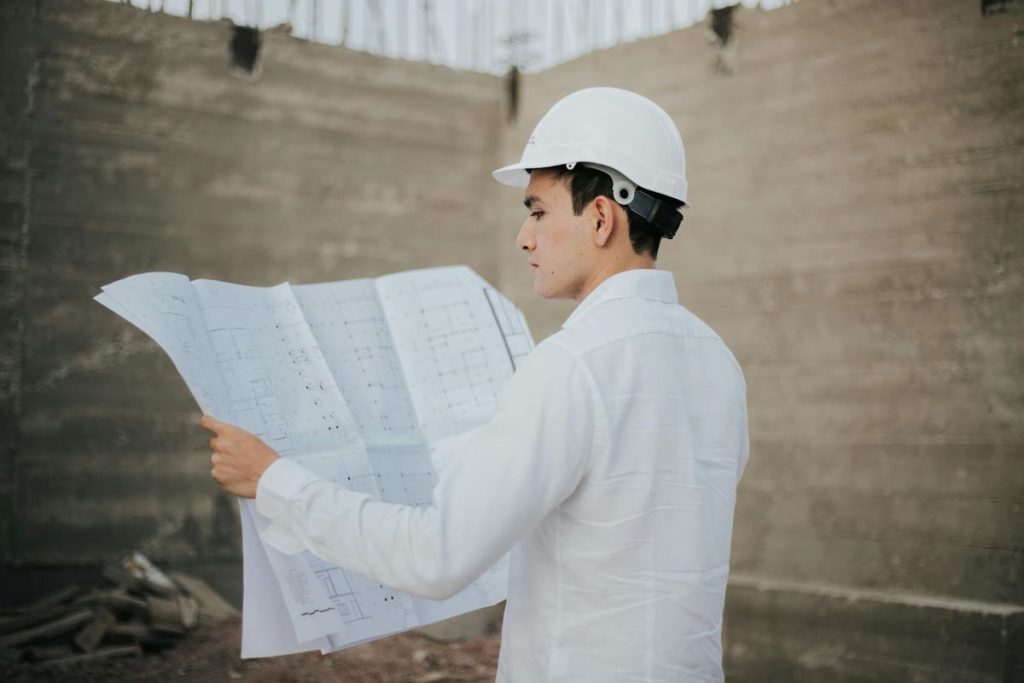 An architect wearing white hat holding on to the traditional and outdated white printed plans on paper.