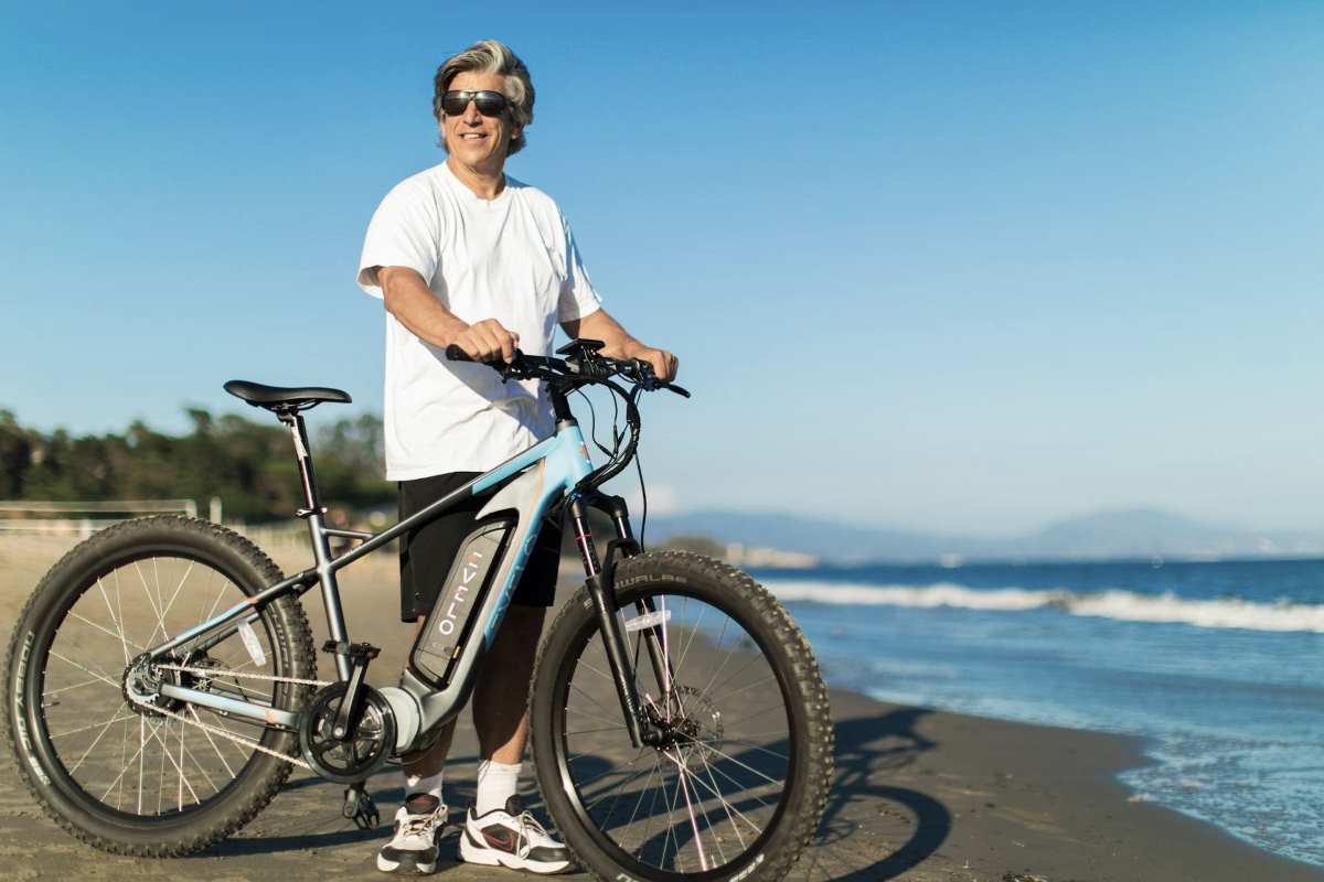 Developing Coastal And Seaside Residences In The Philippines 3 A man holding an electric bicycle stands on a sandy shore with the sea in the background, symbolizing sustainable mobility and the integration of essential amenities near coastal residential areas in the Philippines.