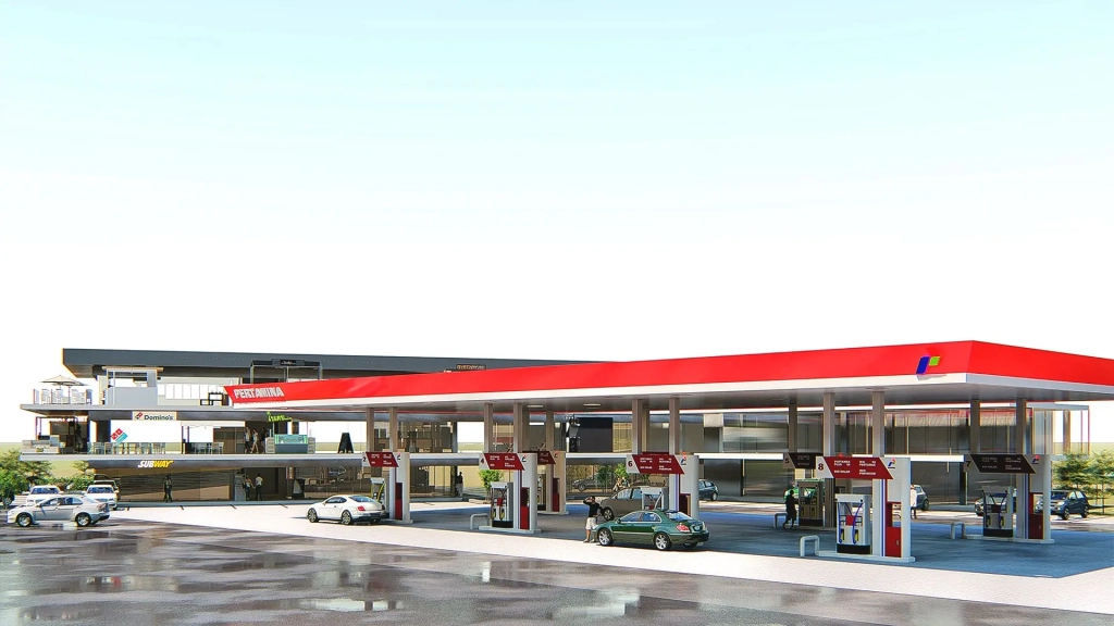 Gas station with wide red canopy, multiple fueling bays, flat-roof retail building behind with three commercial levels, transparent glass facades, parking spaces, and vehicle circulation paths in Calamba City, Philippines.