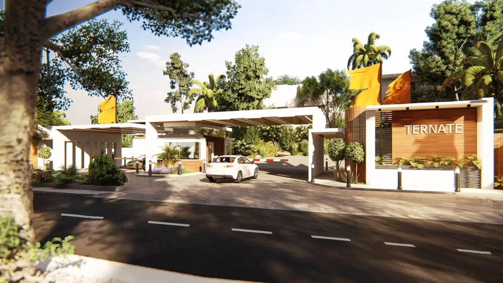 Modern gated entrance of Ternate Coastal Estate featuring white geometric canopy structures, horizontal wood cladding with development name signage, landscaped tropical greenery, vehicle control gates, bollards, paved driveway, and tropical trees surrounding the secure community entrance.